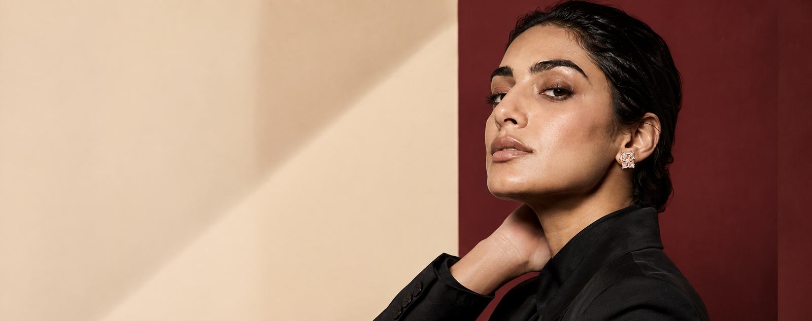 Model wearing Solaire gold diamond studs against a maroon wall
